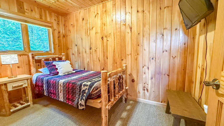 Snuggle into this cozy cabin bedroom where warm wood surrounds you and forest views greet your morning through charming windows.