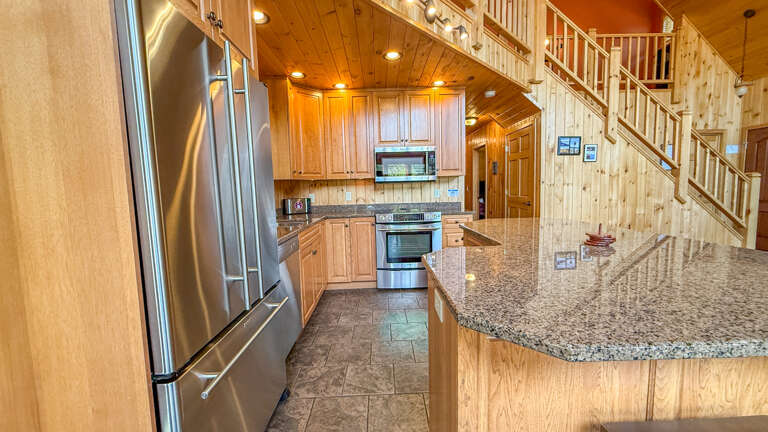 Step into your cabin's open-concept kitchen, where sleek granite counters, stainless appliances, and warm wood finishes blend comfort with convenience for memorable mountain meals.