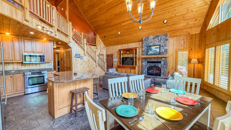 Step into this soaring lodge-style retreat where rustic wood beams and a stone fireplace create warmth. Gather around the dining table, whip up meals in your fully-equipped kitchen, and unwind in the open living space.