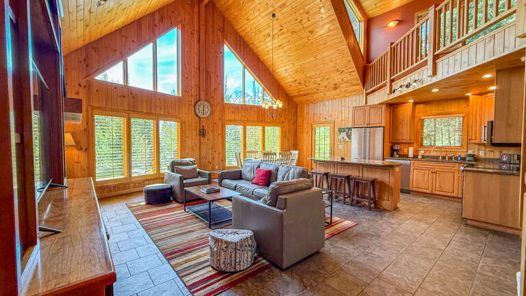 Sunlight floods through soaring windows, warming the open living area where you can relax on plush seating or gather at the kitchen bar beneath vaulted wood ceilings.