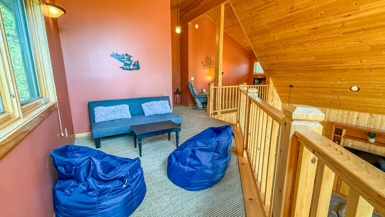 Unwind in your cozy loft lounge with vibrant bean bags, a sleek futon, and warm wood tones that wrap you in cabin comfort.
