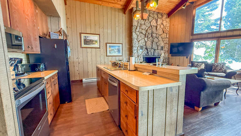 Gather around your spacious kitchen island and feel the warmth of the stone fireplace while natural light pours through towering windows, framing peaceful forest viewsâyour cozy retreat awaits.