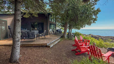 A stunning waterfront property situated directly on the shoreline, where towering pines frame a private deck and red Adirondack chairs invite you to soak in tranquil lake views.
