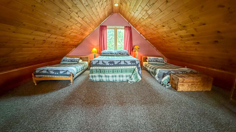 Rest peacefully in this cozy loft bedroom with rustic wood beams and charming wildlife-themed bedding for your mountain getaway.