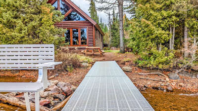 A rustic log cabin nestled among towering pines, with accessible walkway and outdoor seating for peaceful forest moments.
