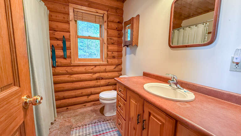 Step into your rustic bathroom featuring warm log walls, polished countertops, and natural light streaming through the window.
