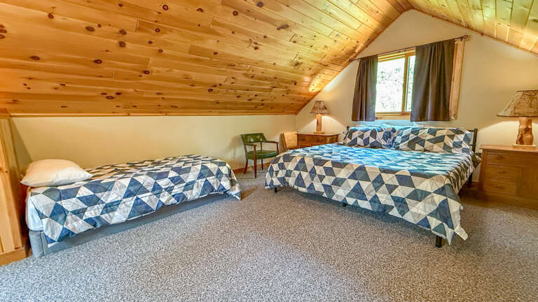 Cozy attic bedroom with rustic wooden ceiling beams and twin beds featuring vibrant geometric bedding for your peaceful mountain retreat.