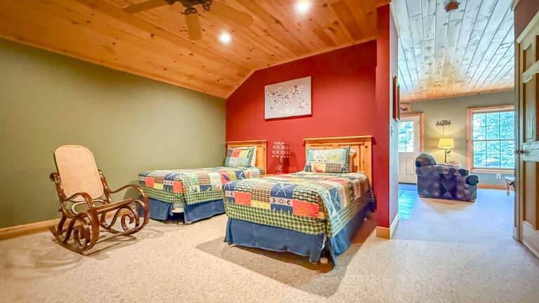 Your cozy retreat features two twin beds with colorful quilts and warm wood-paneled ceilings, perfect for peaceful nights after a day of adventure. A charming rocking chair invites you to relax and unwind.