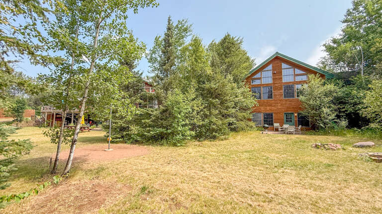 A distinctive cabin-style building with a green roof nestles into mature woodlands, offering natural seclusion and charm. Additional structures visible on the property suggest a spacious retreat.
