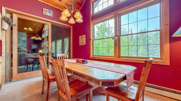 Gather around this handcrafted dining table in a space bathed in natural light, where bold red walls and forest views through expansive windows create a warm, inviting atmosphere for your meals.