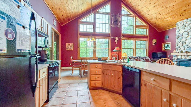 Picture yourself cooking in this bright, open-concept kitchen with its vaulted wood ceiling, natural light streaming through floor-to-ceiling windows, and cozy stone fireplace anchoring your mountain retreat.