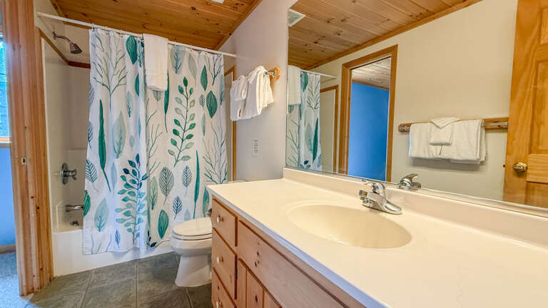 Step into your bright, cabin-style bathroom where fresh towels and a soothing leaf-patterned curtain set the tone for a peaceful stay. Everything you need is right here, ready for your arrival.