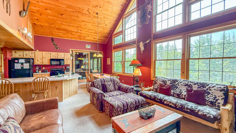 Step into this rustic mountain retreat with soaring windows, vaulted pine ceilings, and rich red walls. The open-concept living area offers stunning forest views, a fully equipped kitchen, and the perfect cozy atmosphere to unwind.