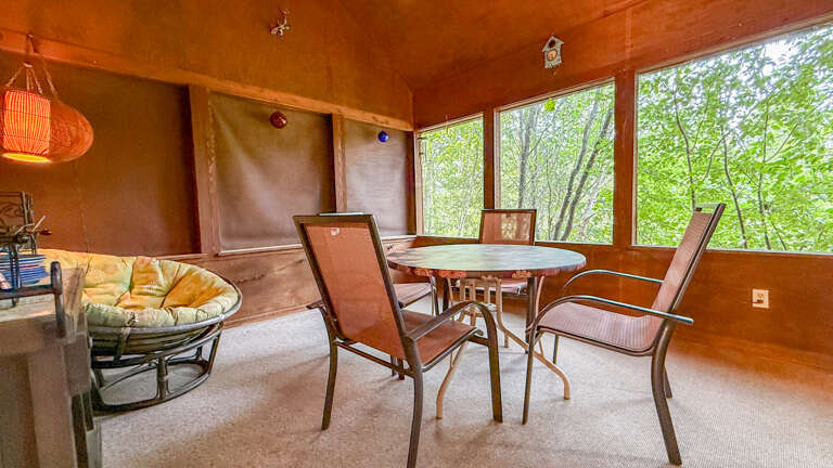 Step into your sunlit retreat where warm wood tones and floor-to-ceiling windows frame lush greenery right outside your door. Gather around the table or sink into the cozy papasan chairâyour peaceful escape awaits.