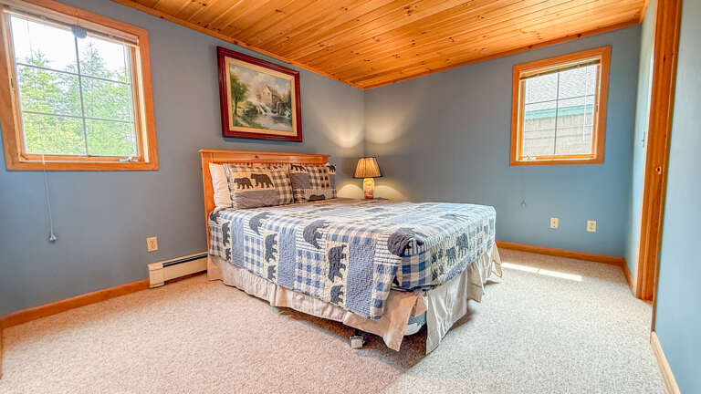 Unwind in your cozy bedroom with a plush bed, warm wood ceiling, and soft natural light. Rustic decor and peaceful blue-gray walls help you relax at the end of your day.