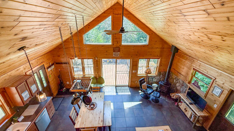 Soaring ceilings and warm wood tones create an inviting great room where you can gather around the cozy wood-burning stove or enjoy natural light streaming through expansive windows overlooking the deck.