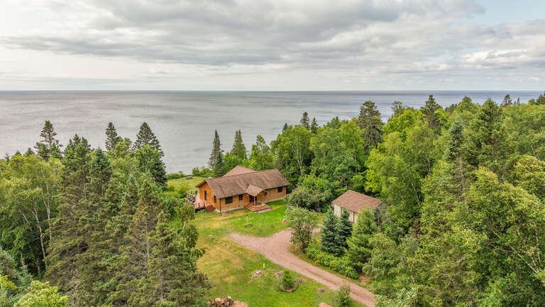 Aerial view captures the property's tranquil lakeside setting, surrounded by lush forest and offering direct access to Lake Superior's shoreline.