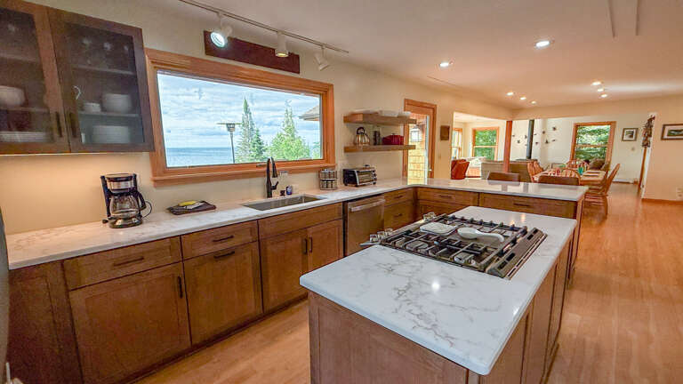 Cook up your favorite meals in this spacious gourmet kitchen, featuring sleek marble countertops, modern gas range, and warm wood cabinetryâall while enjoying stunning water views through the wide picture window above the sink.