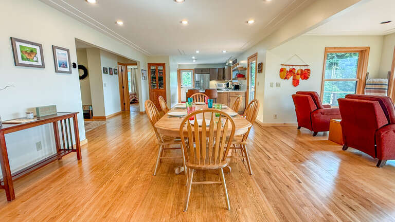Gather around the dining table in this open, sunlit space where natural light streams through the windows. The warm hardwood floors flow seamlessly from dining to kitchen to living area, creating a welcoming home for your mountain getaway.