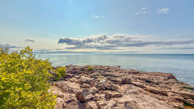 Coastal natural landscape featuring rocky shoreline and calm waters under expansive skies.