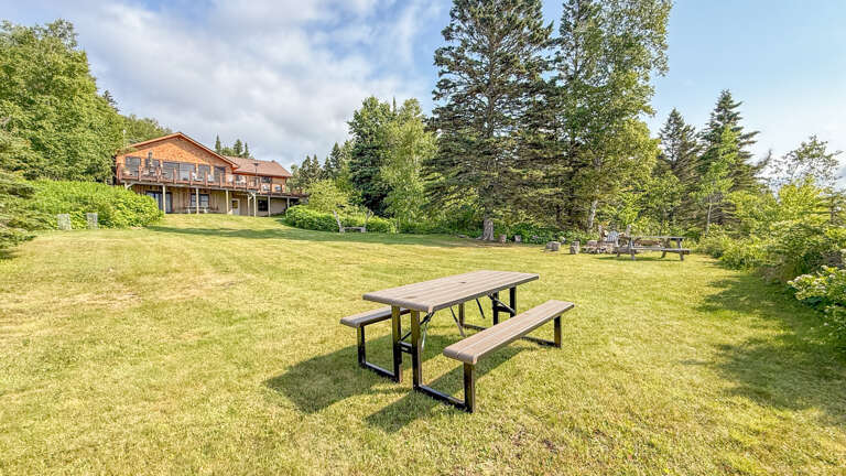 The property sits on a spacious, sun-drenched lawn surrounded by mature evergreens, offering a peaceful retreat in a natural wooded setting.