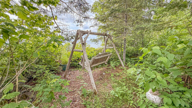 The property features a peaceful natural landscape with wooded garden areas. A rustic wooden swing provides a tranquil retreat surrounded by mature trees and native plantings, offering a quiet connection to nature during your stay.