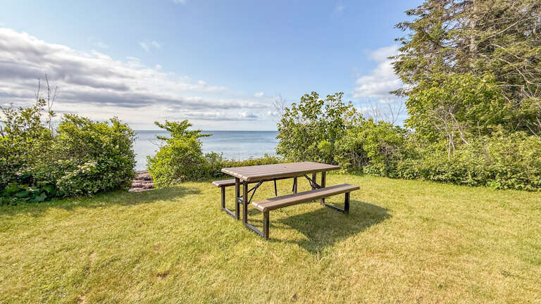 A beautifully maintained property with lush green lawn leading to stunning waterfront scenery, framed by natural vegetation and open skies.