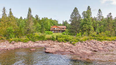 A serene lakeside retreat nestled among towering pines and lush greenery, with waterfront views and natural rock formations defining the peaceful shoreline.