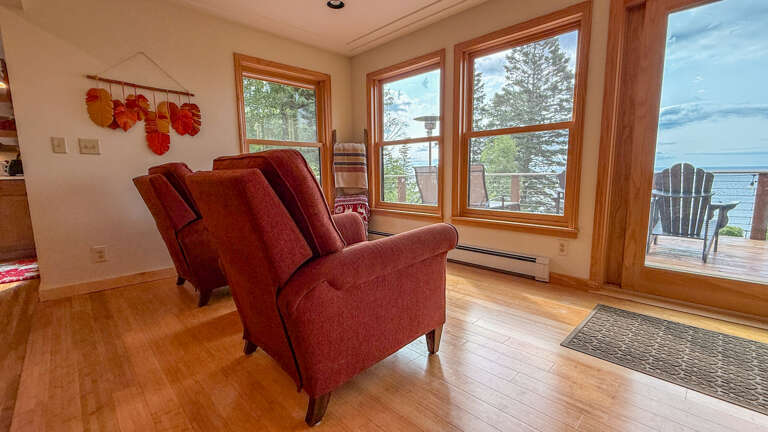 Sink into these plush chairs and let your gaze drift across the shimmering water stretching to the horizon. Natural wood tones and warm accents create a cozy retreat where every window frames your own private waterfront escape.