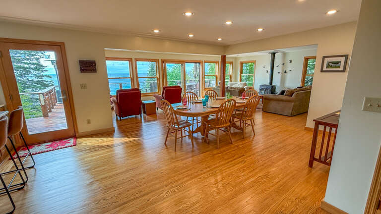 Spacious open-concept living area with gleaming hardwood floors, comfortable seating, and stunning lakeside views through expansive windows.