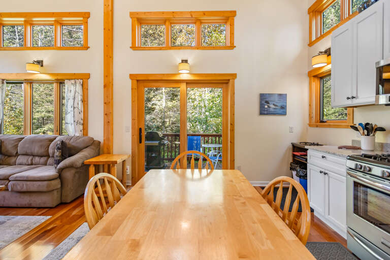 Gather around this inviting dining space where soaring ceilings and floor-to-ceiling windows bathe your meals in natural light. The open layout seamlessly connects your living and cooking areas to a private deck surrounded by trees.