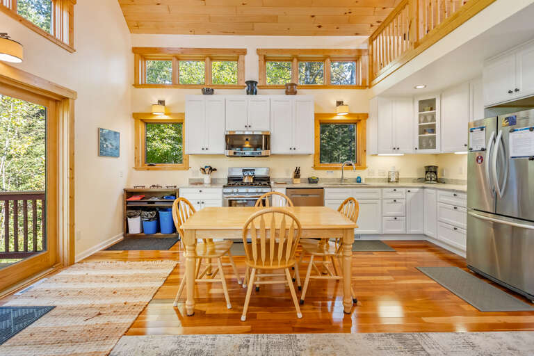 Your bright, open kitchen invites you to gather around the farmhouse table, where natural light streams through tall windows and a warm wood ceiling adds rustic charm overhead.
