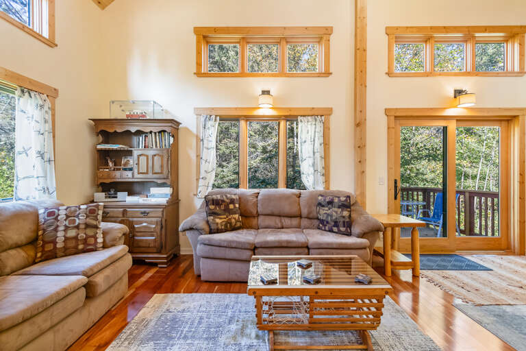 Relax in your spacious living room with soaring ceilings, cozy leather sofas, and stunning views of the surrounding forest through floor-to-ceiling windows and your private deck.