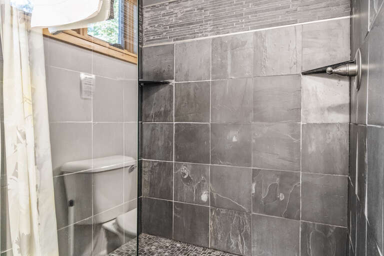Step into your beautifully tiled walk-in shower, where elegant gray stone and a refreshing rainfall showerhead create a modern spa-like retreat after your day of exploring.