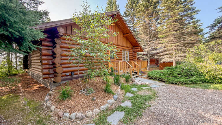 A classic log cabin nestled among towering evergreens, offering a peaceful mountain retreat with natural wood charm and welcoming outdoor space.