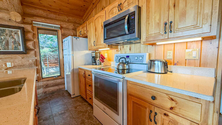 Your fully equipped cabin kitchen offers everything you need to cook up delicious meals, with modern appliances nestled in warm wood cabinetry and views of the surrounding forest just steps away.