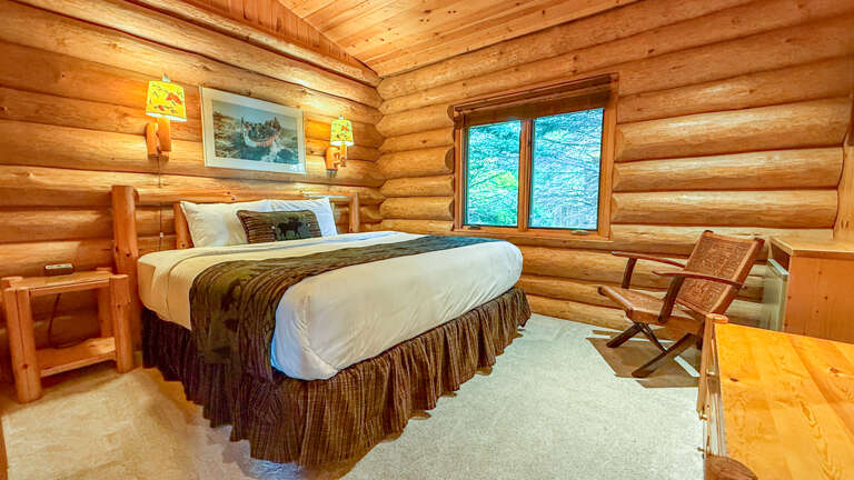 Relax in your cozy log cabin bedroom, where warm timber walls and soft lighting create an intimate retreat. Wake up to natural beauty framed through the window and unwind in rustic charm.