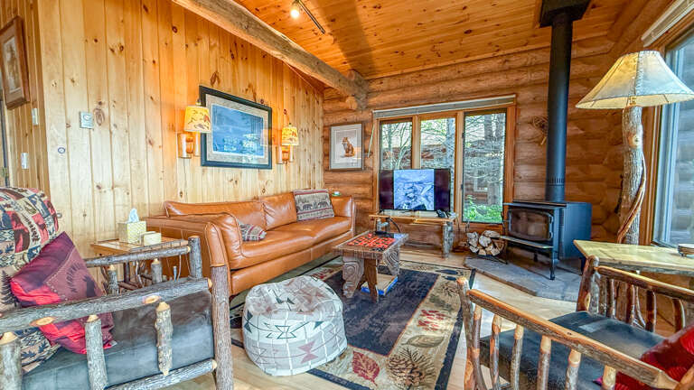 Sink into rustic comfort in your cozy cabin living room, where warm wood surrounds you, a wood-burning stove crackles nearby, and handcrafted details invite you to unwind after a day of mountain adventure.