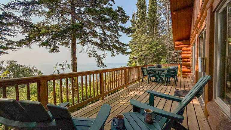 A tranquil lakeside cabin retreat featuring a spacious wooden deck surrounded by towering pines and serene waterfront views. Comfortable Adirondack chairs invite quiet mornings with coffee.