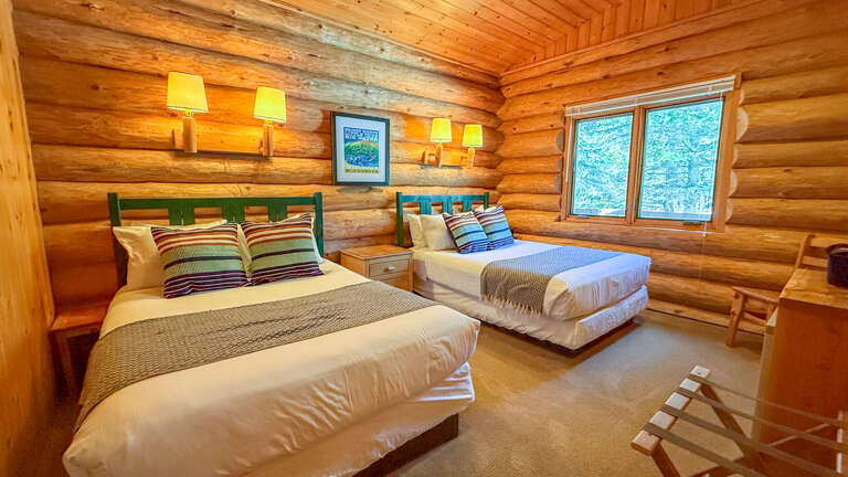 Cozy log cabin bedroom with colorful striped bedding and warm wood walls creating your perfect mountain retreat sanctuary.