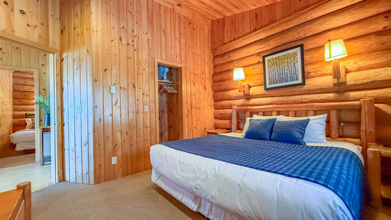 Drift into peaceful slumber in your cozy log cabin bedroom, where warm wood walls and soft lighting create the perfect mountain retreat atmosphere.