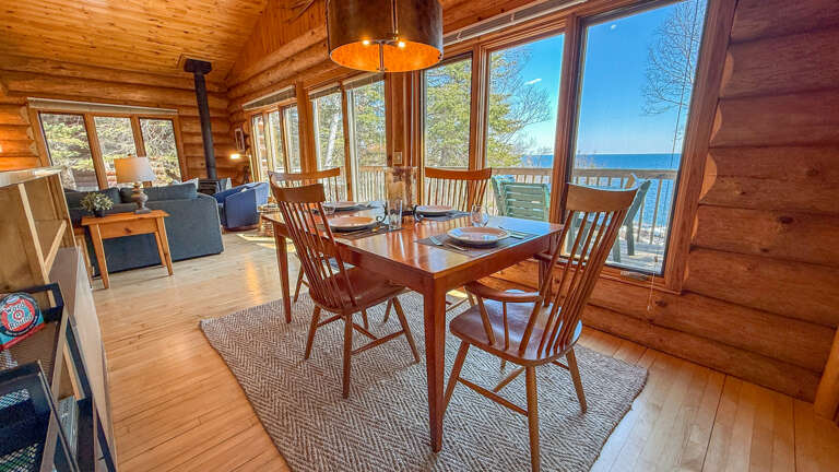 Gather around the handcrafted dining table where warm wood meets stunning lake views through floor-to-ceiling windows.