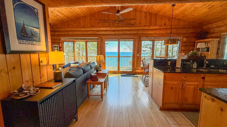 Your lakefront cabin offers an open living space where rustic wood meets modern comfort, with stunning water views streaming through panoramic windows.