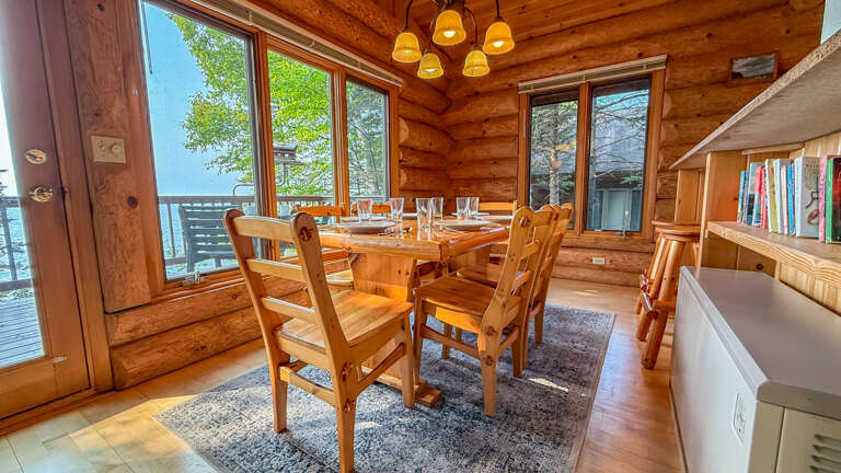 Gather around this handcrafted log dining table with warm wood tones embracing you from every angle. Sunlight streams through panoramic windows, framing forest views that invite you to relax and connect over memorable meals.