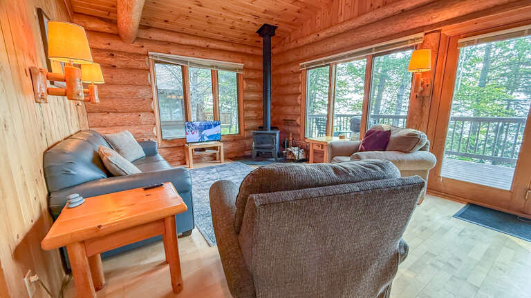 Settle into this warm, wood-wrapped living space where your mornings unfold around the crackling wood stove. Step through those doors to your balcony and let the surrounding forest become your private backdrop.