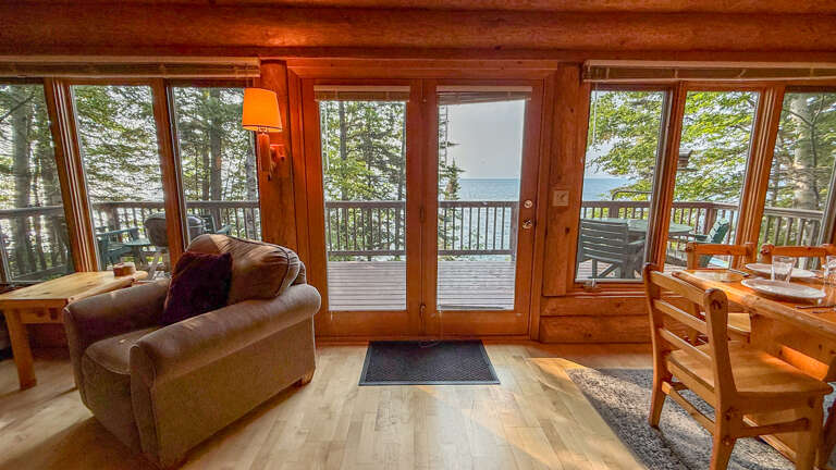 Step into your cozy lakeside retreat where floor-to-ceiling windows frame stunning water views. Warm wood tones and comfortable furnishings invite you to relax while nature surrounds your private deck.