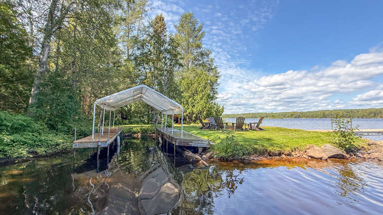 The property features a private dock and waterfront access on a serene lake, with a grassy lawn and Adirondack chairs positioned at the water's edge for peaceful lakeside relaxation.