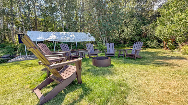 Gather around your private fire pit on this peaceful wooded lawn. Classic Adirondack chairs and covered seating invite you to relax, roast marshmallows, and enjoy the fresh air under towering trees.