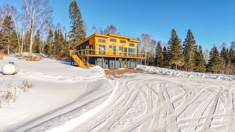 Cross River Cabin is a modern retreat nestled in pristine snow with forest and Lake Superior views.