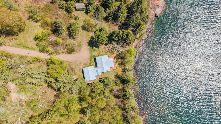 Aerial view of a waterfront property nestled among lush trees along a pristine lake shoreline, offering a secluded and scenic natural setting.
